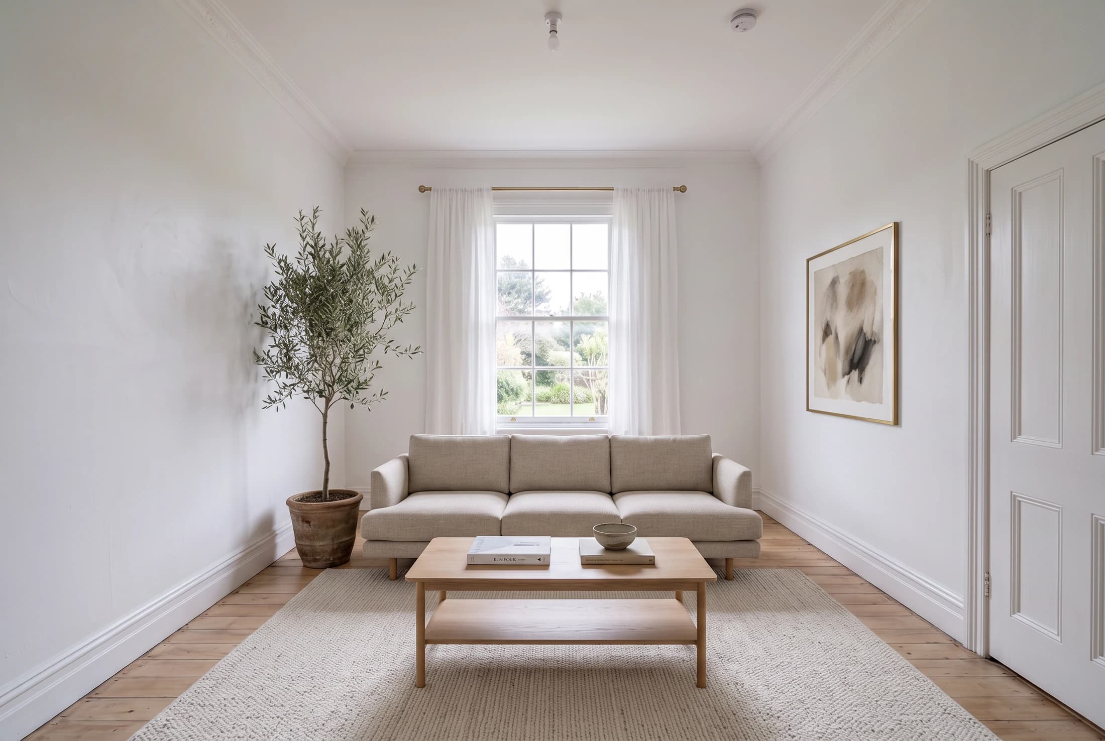 The same living room virtually staged with a linen sofa, rug, coffee table and olive tree